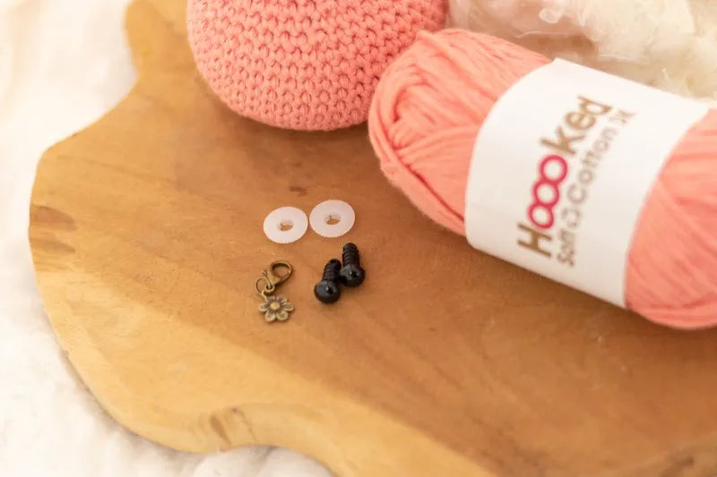 Haakcursus met roze wol, haakbenodigdheden en knoopjes op een houten plank